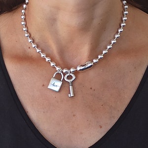 Può includere: Una collana a catena d'argento con un ciondolo a forma di lucchetto d'argento che dice "love" e un ciondolo a forma di chiave d'argento.