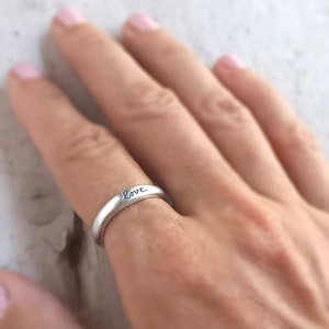 Pu&ograve; includere: Un anello d'argento con la parola "love" incisa sulla fascia.