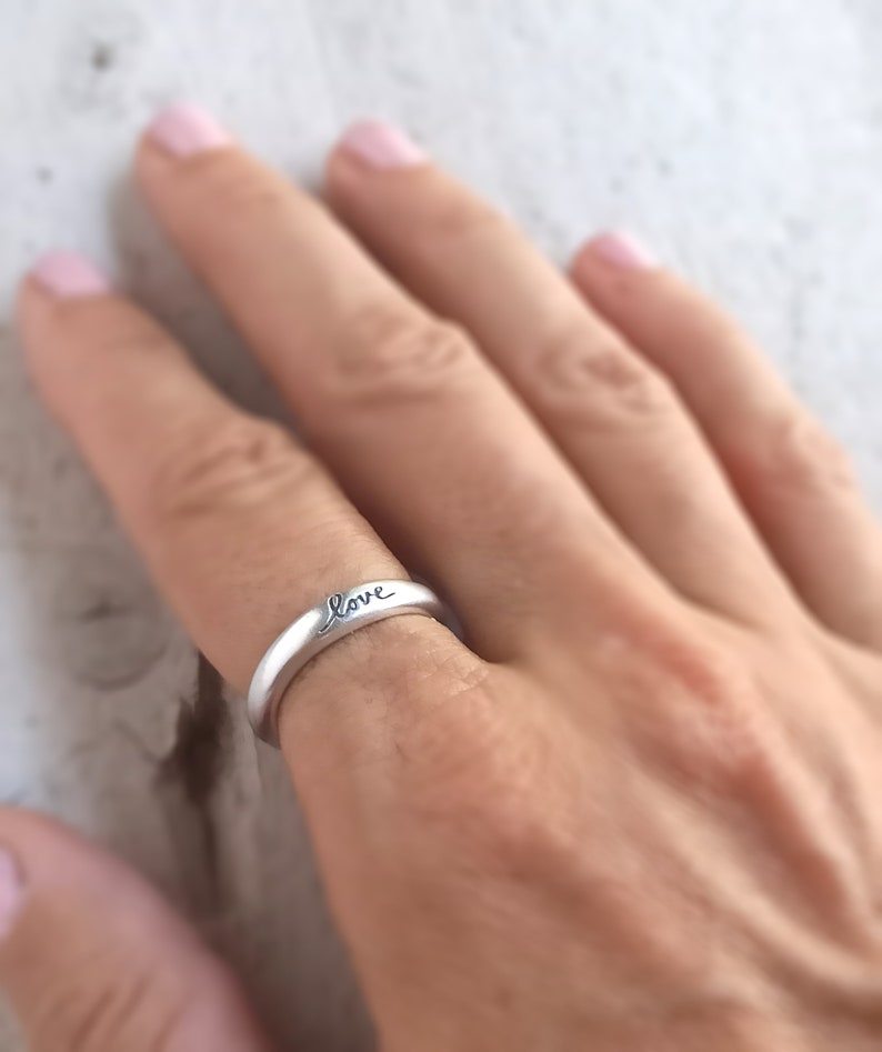 Pu&ograve; includere: Un anello d'argento con la parola "love" incisa sulla fascia.