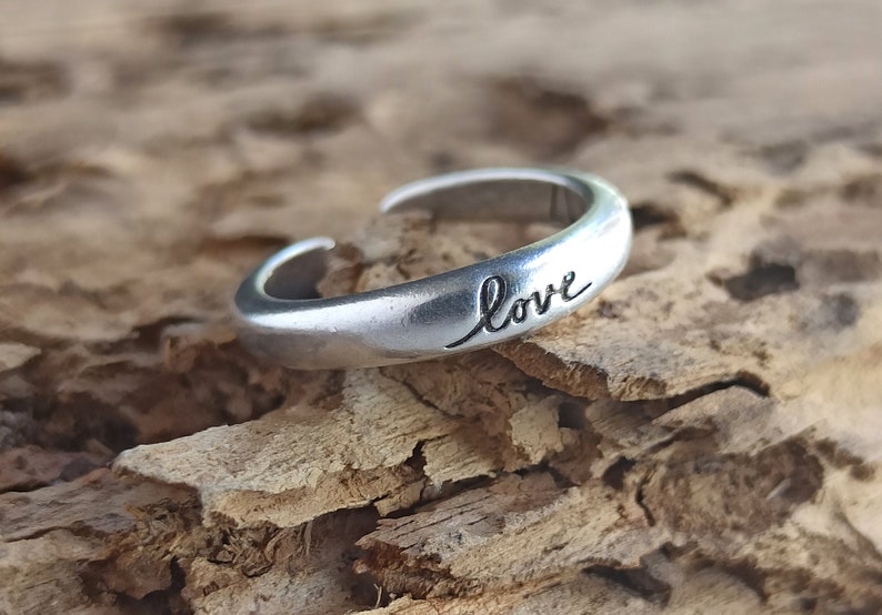 Pu&ograve; includere: Un anello regolabile in argento con la parola "love" incisa sulla fascia.