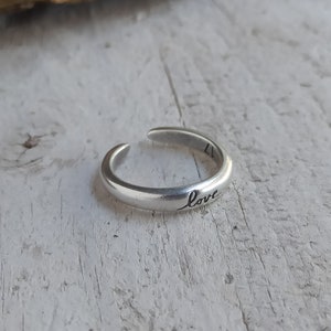 Pu&ograve; includere: Un anello regolabile in argento con la parola "love" incisa sulla fascia.