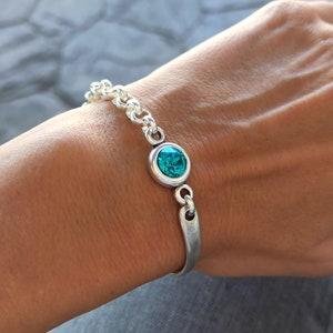 May include: A silver bracelet with a turquoise blue gemstone. The bracelet has a chain link design and a simple, curved bar closure.
