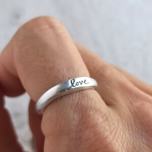 Pu&ograve; includere: Un anello d'argento con la parola "love" incisa sulla fascia.