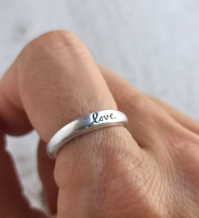Pu&ograve; includere: Un anello d'argento con la parola "love" incisa sulla fascia.