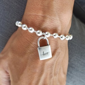 May include: A silver bracelet with a silver padlock charm. The padlock has the word "love" engraved on it.