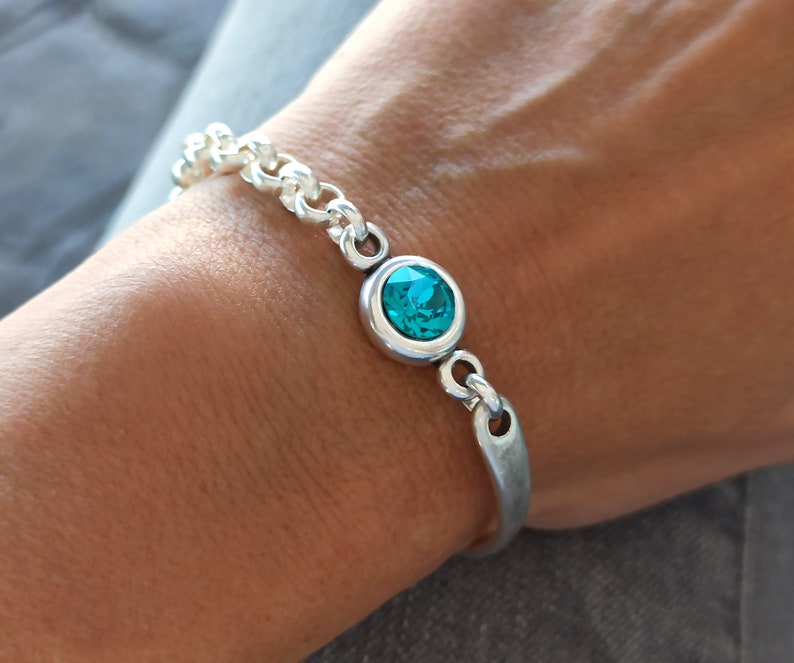 May include: A silver chain bracelet with a turquoise blue gemstone set in a silver bezel. The bracelet has a silver bar clasp.