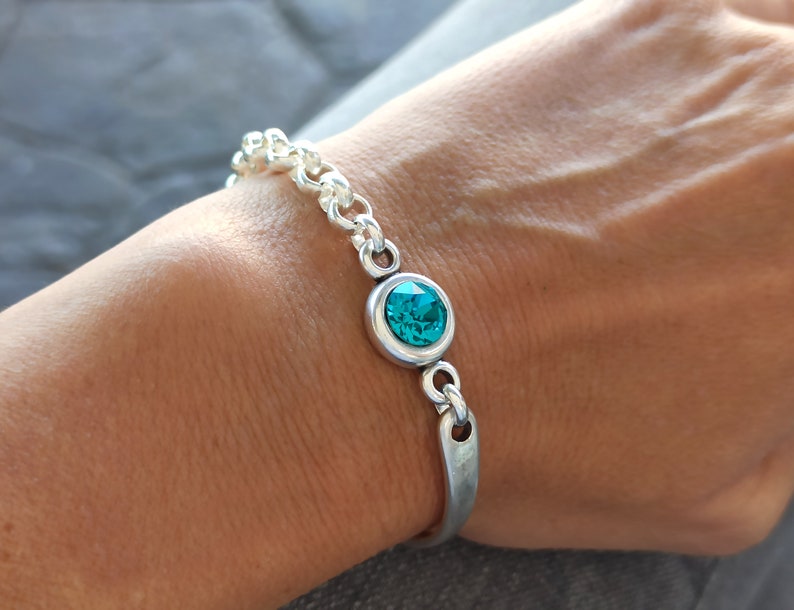 May include: A silver chain bracelet with a turquoise blue crystal accent.