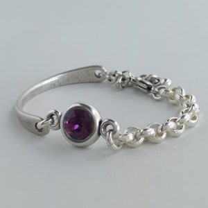 May include: A silver bracelet with a purple gemstone and a chain link design.