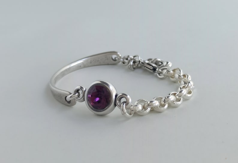 May include: A silver bracelet with a purple gemstone and a chain link design.