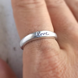Pu&ograve; includere: Un anello d'argento con la parola "love" incisa sulla fascia.