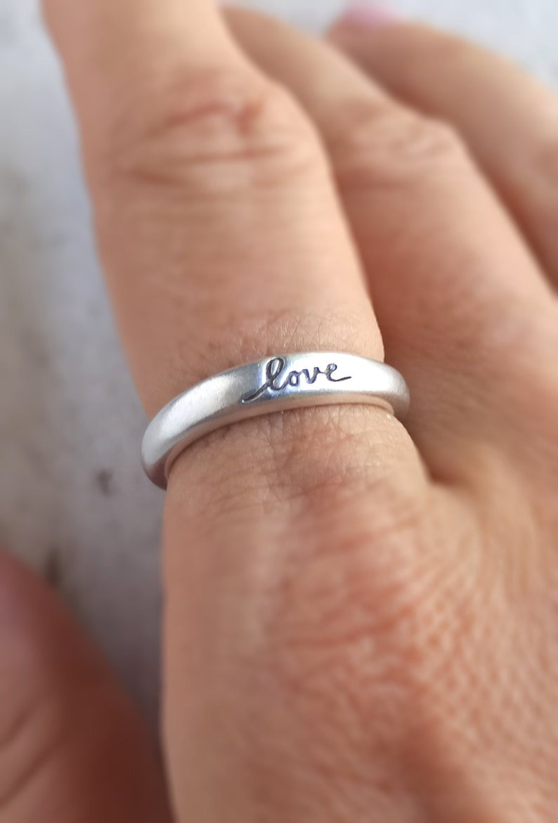 Pu&ograve; includere: Un anello d'argento con la parola "love" incisa sulla fascia.