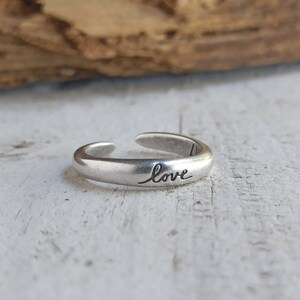 Pu&ograve; includere: Un anello regolabile in argento con la parola "love" incisa sulla fascia.