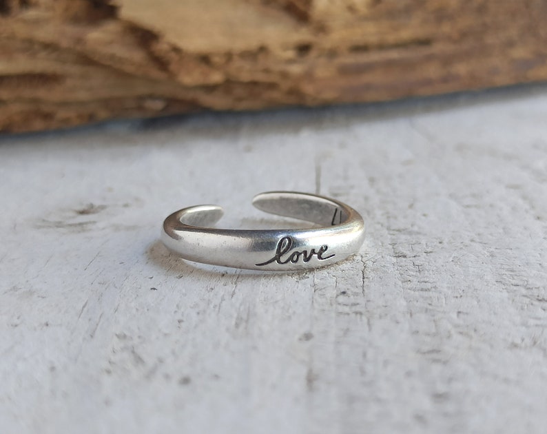 Pu&ograve; includere: Un anello regolabile in argento con la parola "love" incisa sulla fascia.