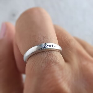 Pu&ograve; includere: Un anello d'argento con la parola "love" incisa sulla fascia.