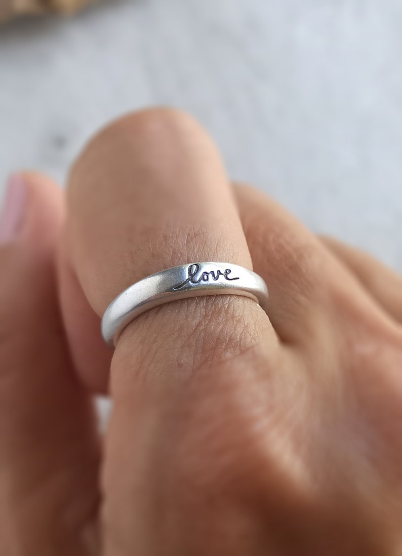 Pu&ograve; includere: Un anello d'argento con la parola "love" incisa sulla fascia.