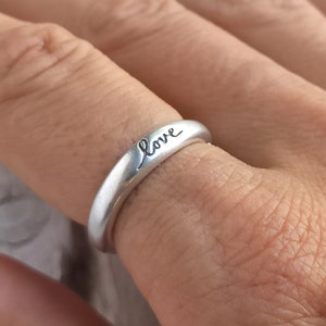 Pu&ograve; includere: Un anello d'argento con la parola "love" incisa su di esso.