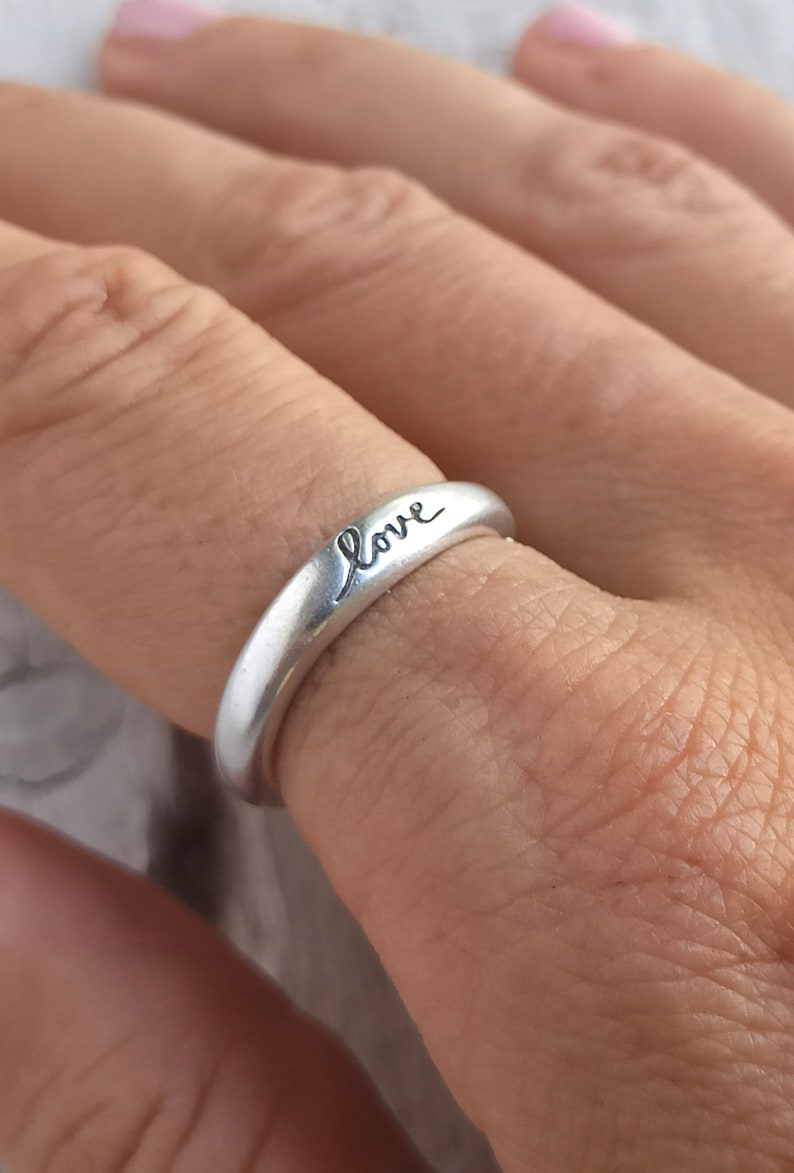 Pu&ograve; includere: Un anello d'argento con la parola "love" incisa su di esso.