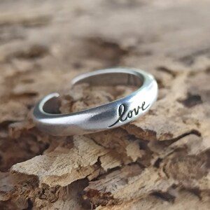 Pu&ograve; includere: Un anello regolabile in argento con la parola "love" incisa sulla fascia.