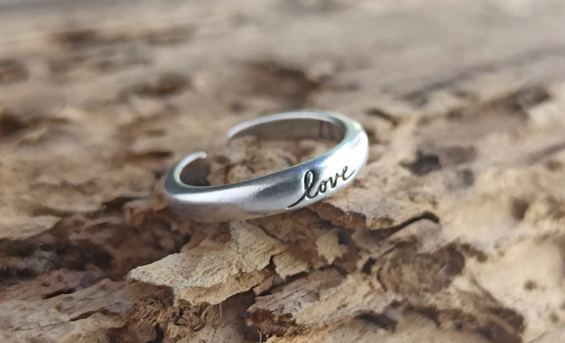 Pu&ograve; includere: Un anello regolabile in argento con la parola "love" incisa sulla fascia.