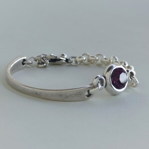 May include: A silver bracelet with a purple gemstone and a clasp closure.