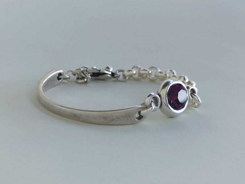 May include: A silver bracelet with a purple gemstone and a clasp closure.