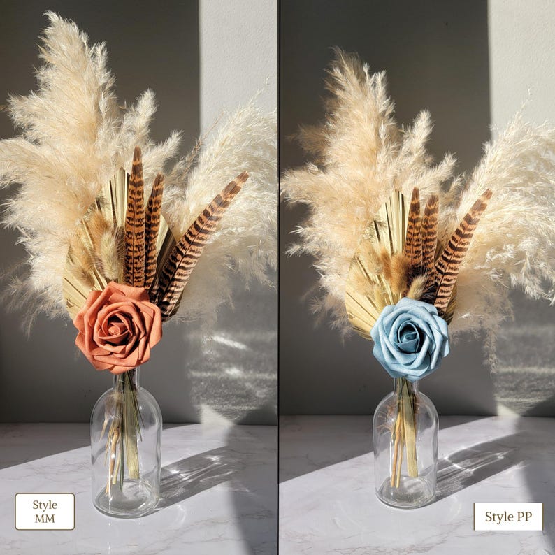 May include: Two dried flower arrangements in clear glass vases. The arrangement on the left features a peach rose and the arrangement on the right features a light blue rose. Both arrangements include dried pampas grass, dried palm leaves, and pheasant feathers. The text "Style MM" is below the left arrangement and the text "Style PP" is below the right arrangement.