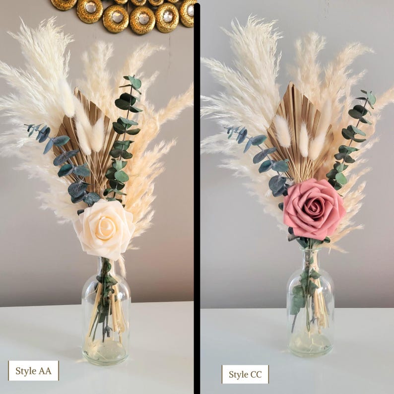 May include: Two arrangements of dried flowers in clear glass vases. The arrangement on the left features a white rose, while the arrangement on the right features a pink rose. Both arrangements include pampas grass, dried palm leaves, and eucalyptus.