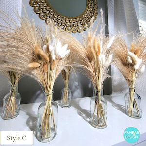 May include: Five clear glass vases filled with dried pampas grass and fluffy white bunny tails. The vases are arranged in a row on a white surface.
