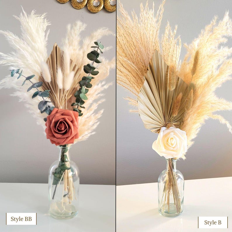 May include: Two arrangements of dried pampas grass, dried palm leaves, and faux flowers in clear glass vases. The arrangement on the left features a peach-colored rose and the arrangement on the right features a white rose. The text "Style BB" is below the left arrangement and the text "Style B" is below the right arrangement.