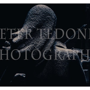 Könnte beinhalten: Nahaufnahme einer verwitterten, grauen Steinstatue einer Person, deren Kopf von der Kamera abgewandt ist. Die Statue ist teilweise von Schatten verdeckt und scheint sich im Freien zu befinden.