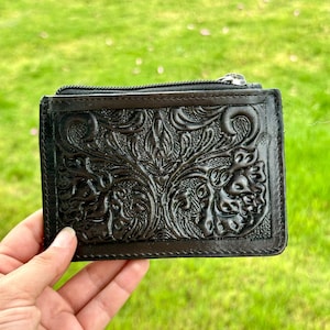 Peut inclure: Un portefeuille en cuir noir avec un motif floral gaufré complexe et une fermeture à glissière.