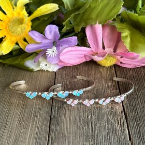 May include: Two silver bracelets with a row of heart-shaped opal stones. One bracelet has blue opal stones and the other has pink opal stones.