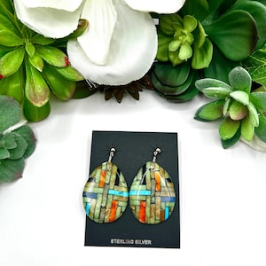 May include: A pair of teardrop-shaped dangle earrings featuring a mosaic pattern of inlaid stone segments in shades of orange, turquoise, black, and tan. The earrings are attached to a black display card labeled STERLING SILVER.