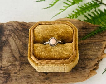 May include: A delicate ring with a pink gemstone set in a silver band, displayed in a yellow velvet ring box.