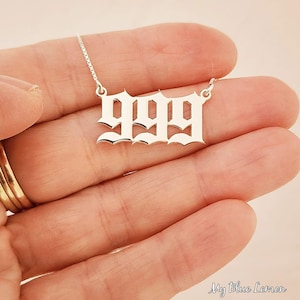 Könnte beinhalten: Silberkette mit einem Anhänger in Form der Zahl 999 in einer gotischen Schrift.