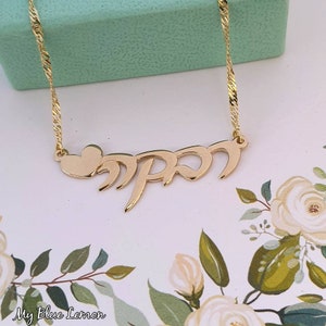 Peut inclure: Collier en or avec un pendentif en forme de cœur et le mot hébreu "mama" en écriture cursive.