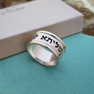 May include: A silver ring with the Hebrew words "Chai" engraved on it. The ring is on a light blue background.