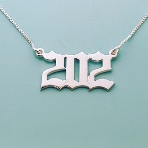 May include: Silver necklace with a pendant in the shape of the year 2022 in a gothic font.