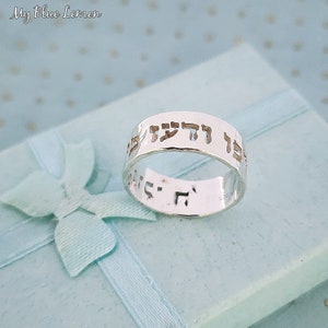 May include: A silver ring with Hebrew text engraved on the band. The ring is on a light blue background with a white bow.