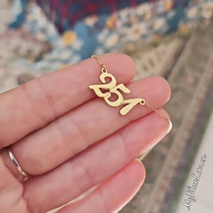 May include: Gold necklace with a pendant featuring the numbers 251 in a stylized font.