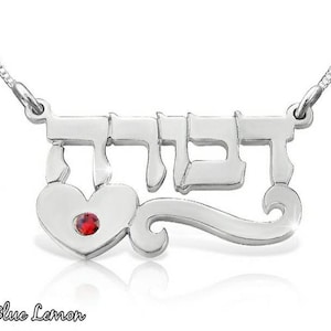 Peut inclure: Collier en argent avec un pendentif en forme de cœur et le mot hébreu "דבורה" en écriture cursive. Le pendentif en forme de cœur est orné d'une pierre précieuse rouge.