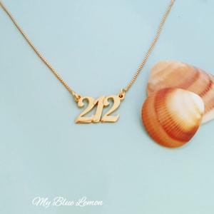 May include: A gold-colored necklace with the number "212" pendant. The necklace is on a light blue background with two seashells. The text "My Blue Lemon" is at the bottom of the image.