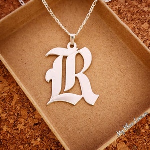May include: Silver necklace with a large, silver, old English letter 'R' pendant.