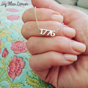 May include: A silver necklace with a pendant featuring the number 1776.