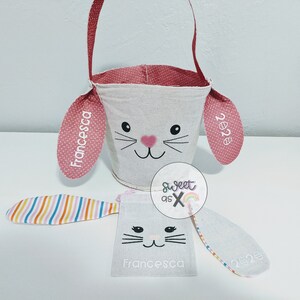 Puede incluir: Una cesta de Pascua de conejito blanca con orejas rosas y un asa rosa. Las orejas est&aacute;n personalizadas con el nombre "Francesca" y el a&ntilde;o "2023".