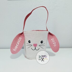 Puede incluir: Una cesta de Pascua blanca con forma de conejo con orejas de lunares rosas. Las orejas est&aacute;n personalizadas con el nombre "Francesca" y el a&ntilde;o "2022".