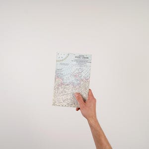 May include: A vintage map of the Soviet Union, held against a white background. The map features detailed geographical information with text in English. The map is rectangular and appears to be folded.