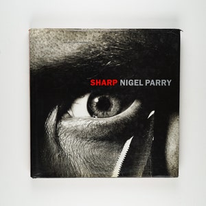 May include: A black and white photo of an eye with a razor blade in front of it. The text "SHARP NIGEL PARRY" is printed in red on the cover of the book.