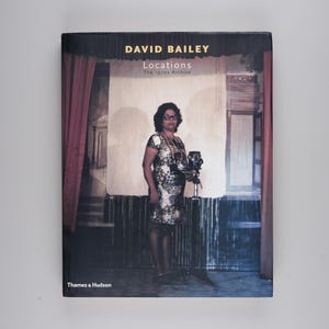 Peut inclure: Couverture de livre avec une photographie d'une femme tenant un appareil photo devant un rideau rouge et une porte en bois. Le titre du livre est "Locations: The Byron Archive" par David Bailey. Le livre est publié par Thames & Hudson.