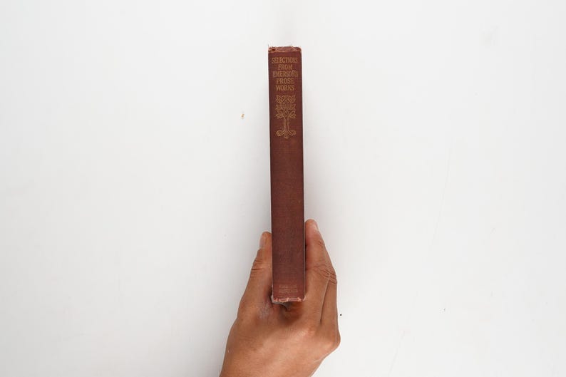 May include: A vintage book with a maroon cover is held in a hand against a white background. The book's spine features gold lettering and decorative elements. The title reads "Selections From Balzac's Prose Works".
